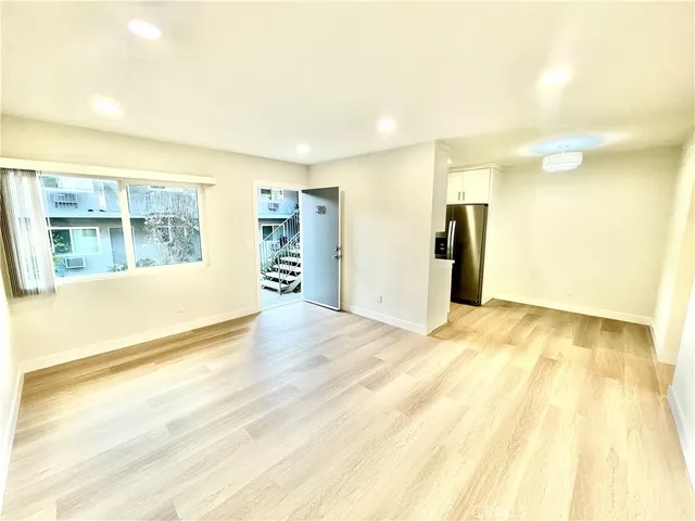 a view of an empty room with wooden floor and a kitchen