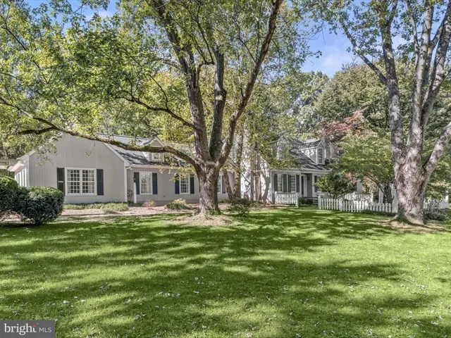 a view of a white house next to a yard with large trees
