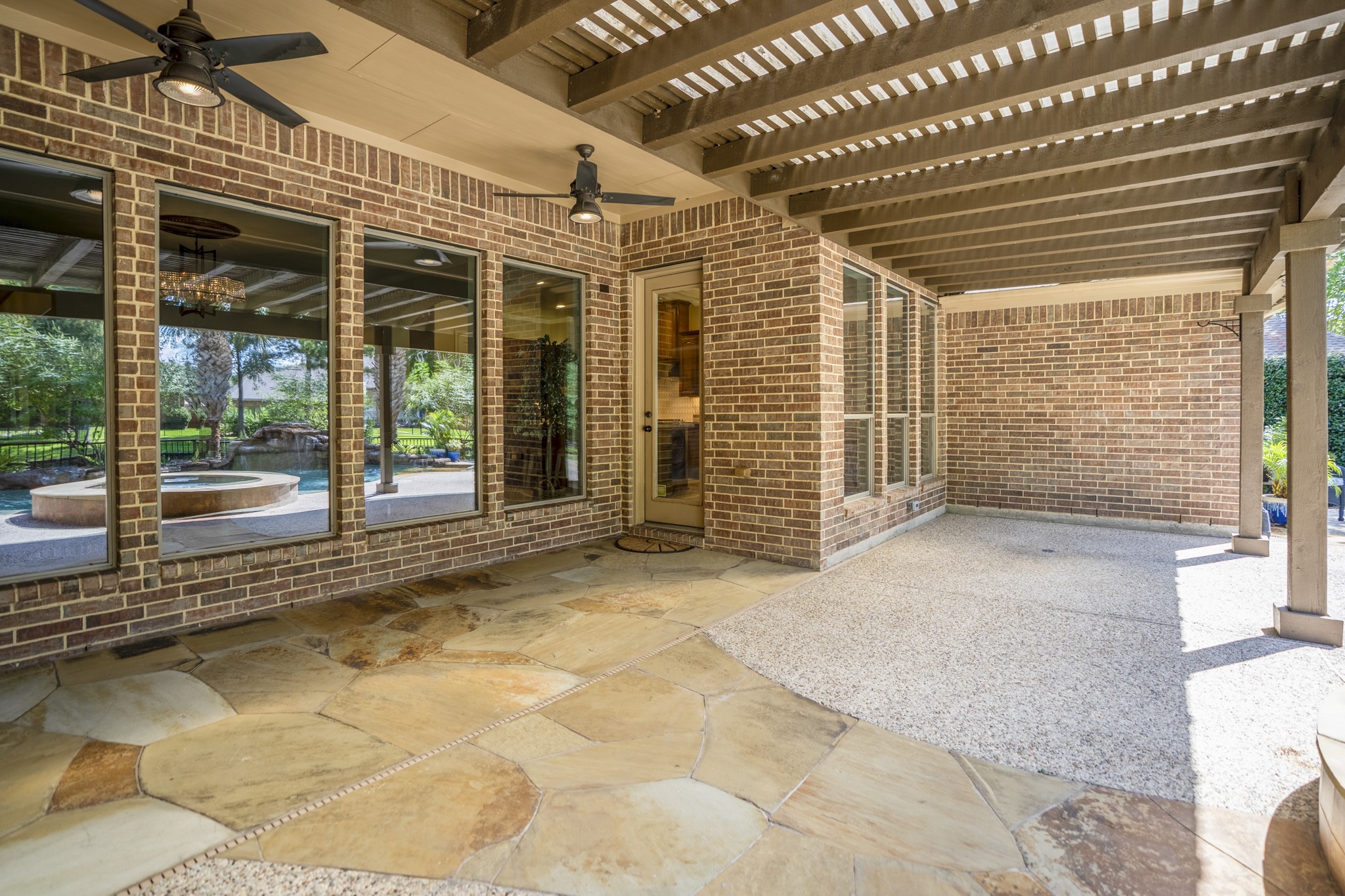 2407 Hendricks Lakes Drive Spring, TX 77388 - Photo 36 of 50 Beneath the 30’ covered pergola, the back patio feels like an outdoor living space made for shaded afternoons, rainy-day coverage, and slower evenings by the water. Stone flooring, substantial support posts, and the covered structure extend the home’s living space outside, while the windows and doors keep the patio connected to the living room and breakfast nook just inside.