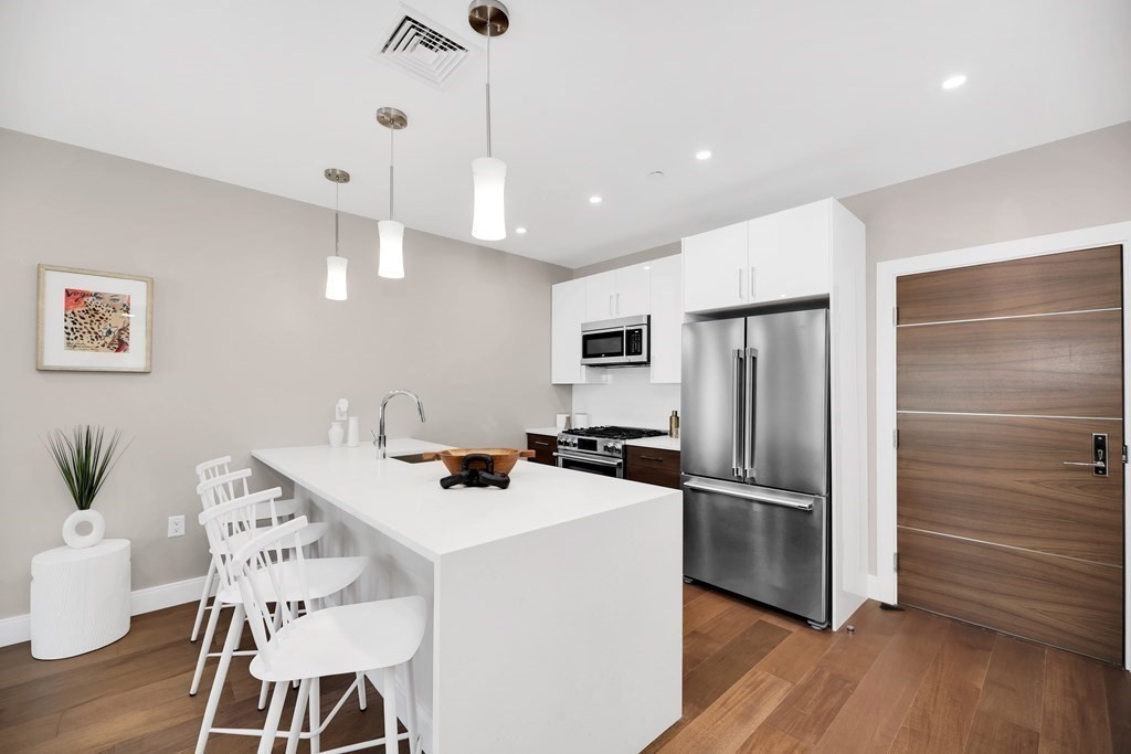 425 Lagrange Street, Unit 109 Boston, MA 02132 - Photo 23 of 42 a kitchen with stainless steel appliances kitchen island granite countertop a refrigerator a stove a sink a dining table and chairs with wooden floor