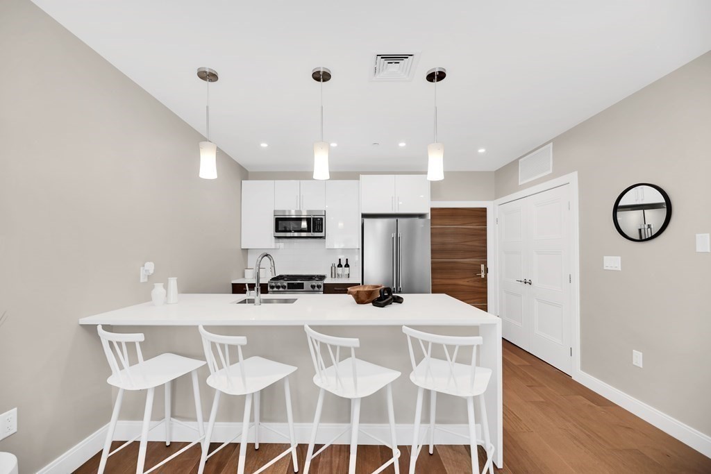 425 Lagrange Street, Unit 109 Boston, MA 02132 - Photo 29 of 42 a kitchen with stainless steel appliances kitchen island granite countertop a dining table chairs and a refrigerator