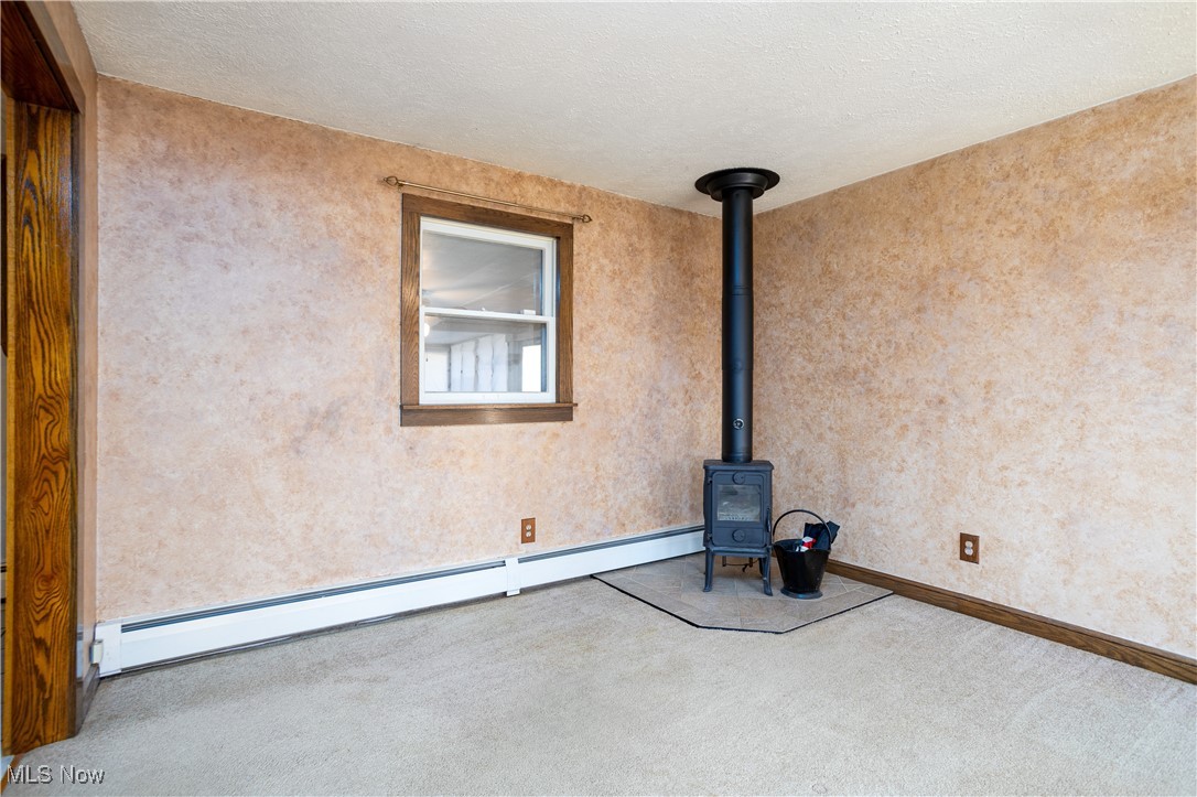 7384 South Cleveland Massillon Road Clinton, OH 44216 - Photo 18 of 35 Unfurnished living room with carpet, a wood stove, baseboard heating, and a textured ceiling and wood burning stove