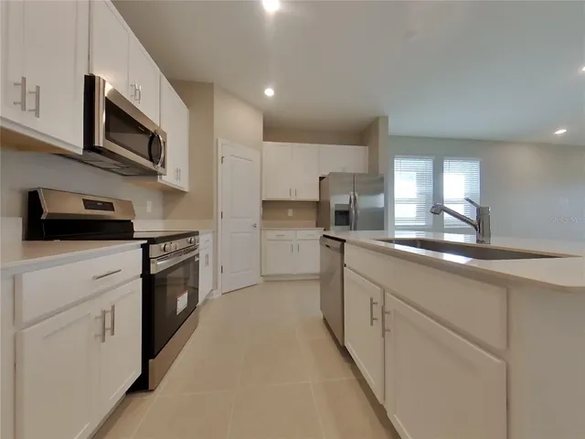 a kitchen with stainless steel appliances granite countertop white cabinets a sink a stove a microwave and a refrigerator