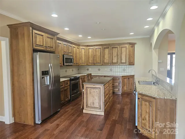 a kitchen with stainless steel appliances granite countertop a refrigerator a stove top oven a sink and dishwasher with wooden floor