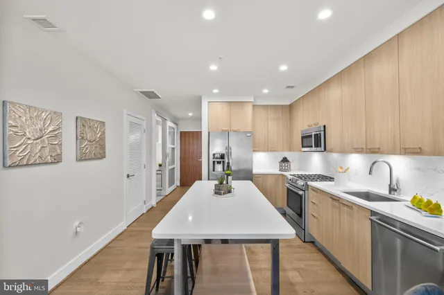 a kitchen with stainless steel appliances kitchen island granite countertop a sink a stove a refrigerator cabinets and a dining table with wooden floor