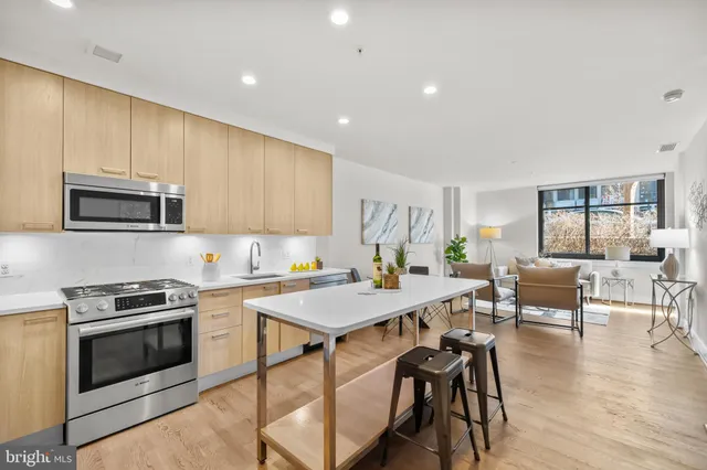 a open kitchen with stainless steel appliances granite countertop a stove top oven a sink a dining table and chairs with wooden floor