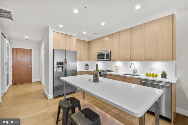 a kitchen with stainless steel appliances a stove a sink a refrigerator white cabinets and wooden floor