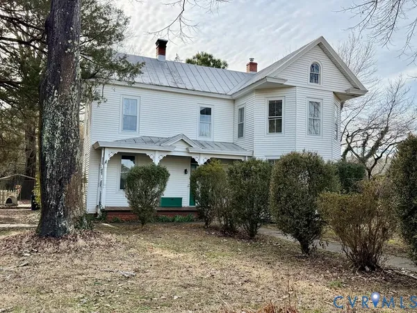a view of a white house next to a yard with large trees