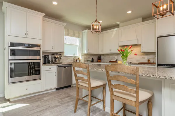 a kitchen with granite countertop a refrigerator a stove a sink and white cabinets with wooden floor