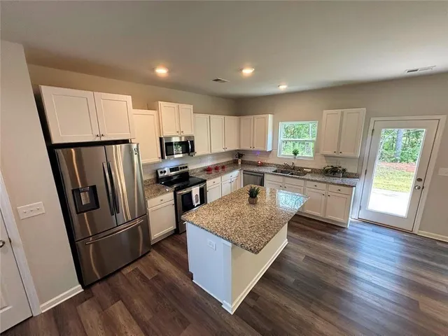 a kitchen with stainless steel appliances granite countertop a refrigerator a sink dishwasher a stove and white countertops with wooden floor