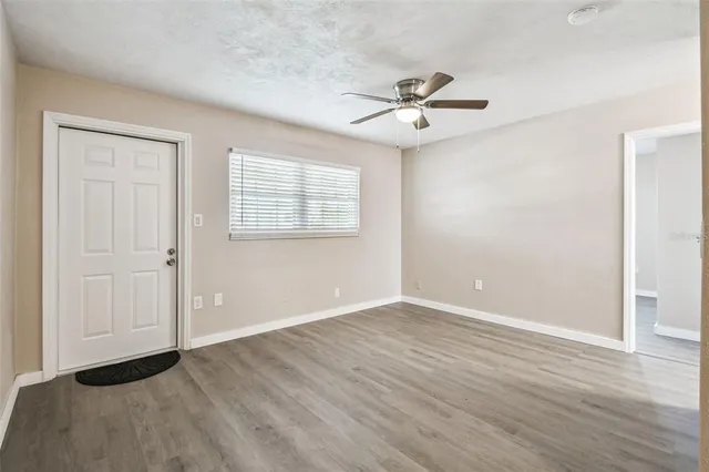 an empty room with wooden floor fan and windows