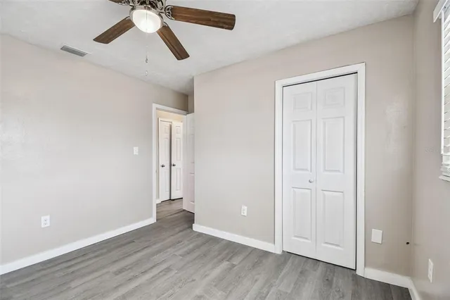 an empty room with wooden floor ceiling fan and windows