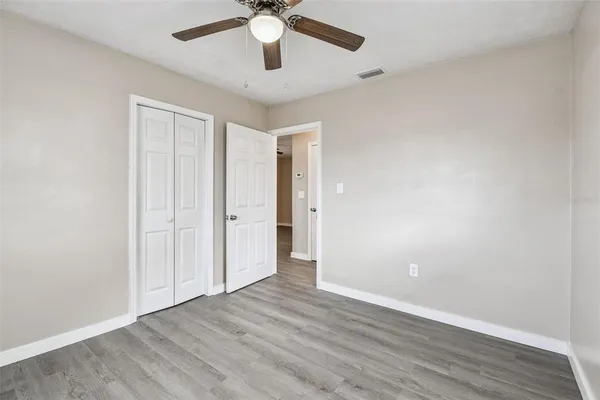 an empty room with wooden floor fan and windows