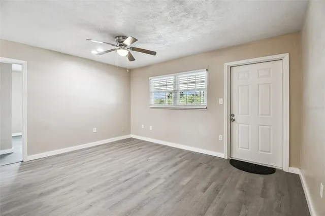 an empty room with wooden floor chandelier fan and windows