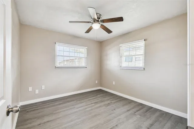 an empty room with wooden floor ceiling fan and windows