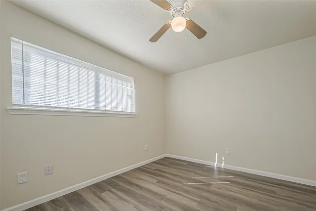 an empty room with wooden floor fan and windows