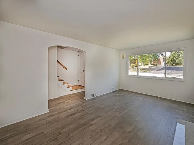 an empty room with wooden floor mirror and windows