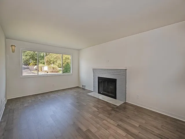 an empty room with wooden floor fireplace and windows