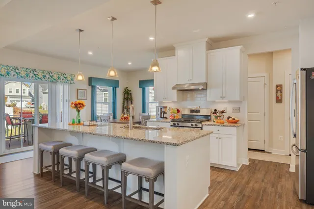 a kitchen with stainless steel appliances granite countertop a stove a sink a refrigerator and chairs with wooden floor