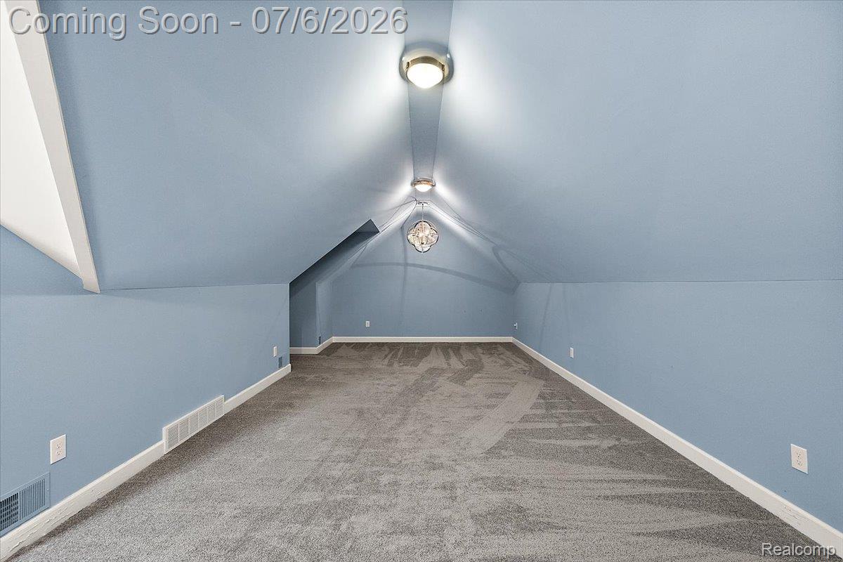 1051 Devonshire Road Grosse Pointe, MI 48230 - Photo 65 of 98 Spacious room featuring sloped ceilings, two ceiling-mounted light fixtures, a decorative ceiling medallion, light blue wall paint, and gray carpeting