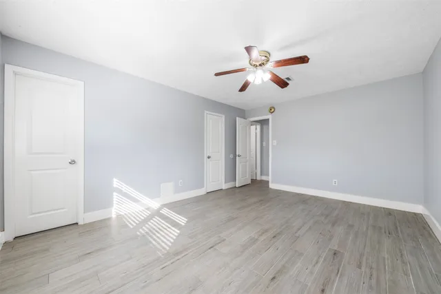 a view of an empty room with wooden floor and a ceiling fan