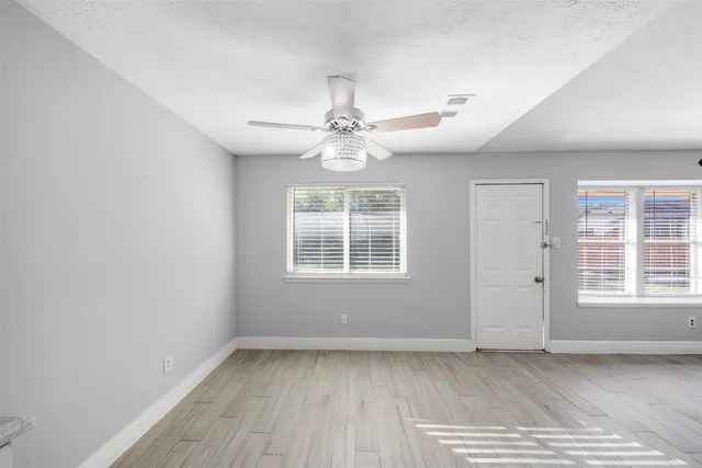 an empty room with wooden floor chandelier fan and windows