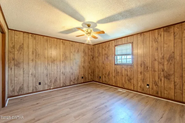 an empty room with wooden floor chandelier fan and windows