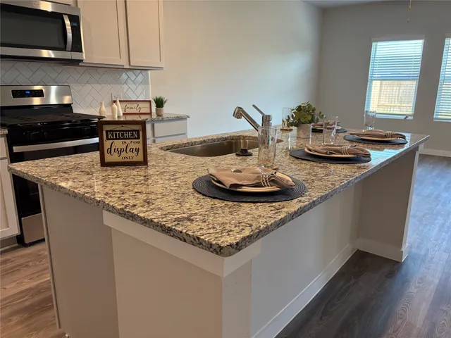 a kitchen with granite countertop kitchen island stainless steel appliances a sink stove and cabinets