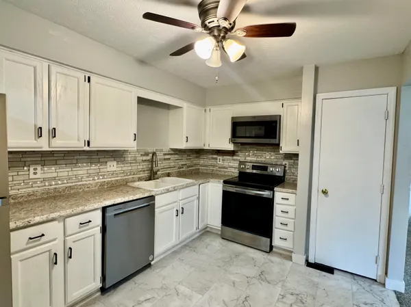 a kitchen with stainless steel appliances granite countertop a refrigerator a stove a sink and white cabinets