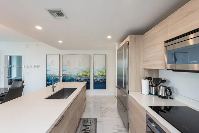 a large kitchen with kitchen island a large counter top space a sink a refrigerator and cabinets