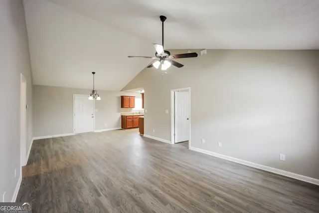 a view of an empty room with chandelier fan and wooden floor