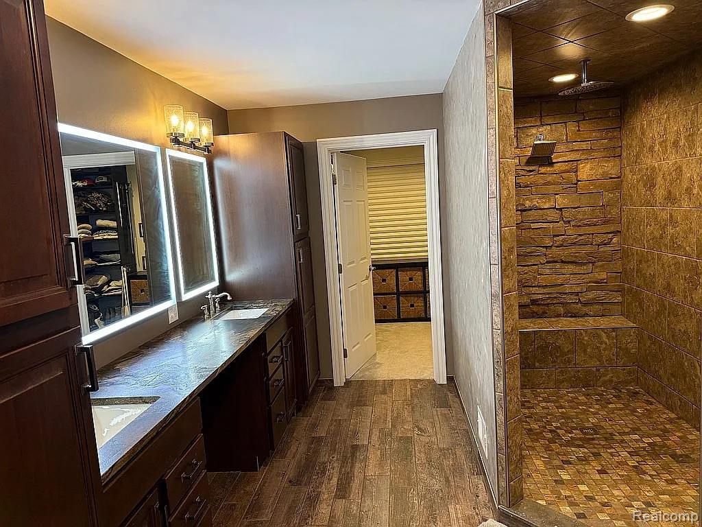 1555 Thompson Road Bad Axe, MI 48413 - Photo 7 of 14 Dual vanity with undermount sinks, wood-finish flooring, custom wood cabinetry, illuminated mirrors, and a stone-tiled shower with a built-in bench