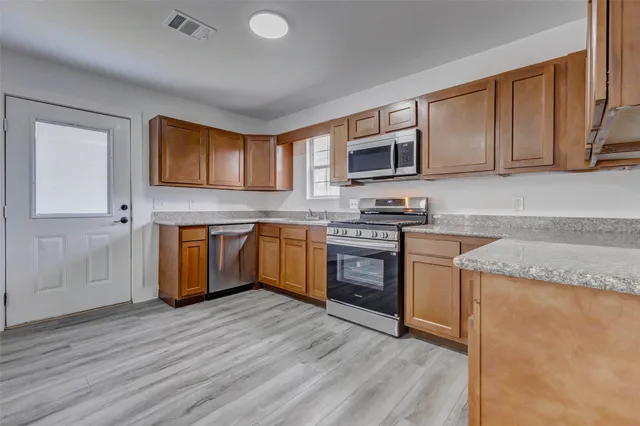 a kitchen with stainless steel appliances granite countertop a stove top oven a sink dishwasher and white cabinets with wooden floor