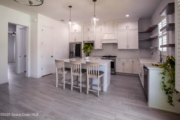 a kitchen with stainless steel appliances granite countertop a white refrigerator a oven a stove and a dining table with wooden floor