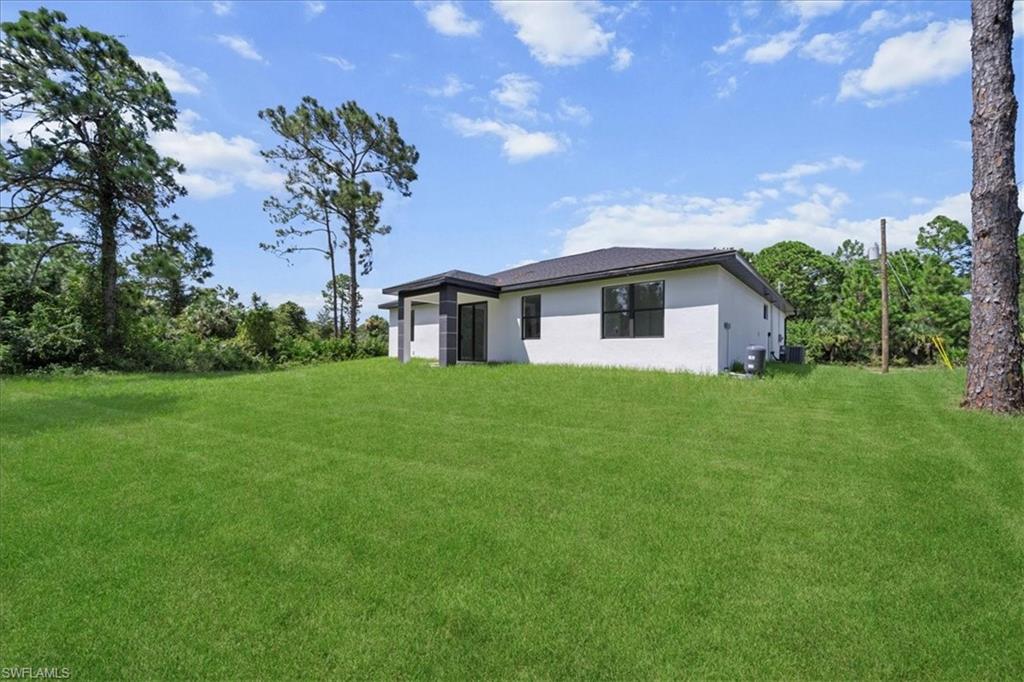 3315 67th Street West Lehigh Acres, FL 33971 - Photo 32 of 38 Back of property with stucco siding, a yard, and an attached garage
