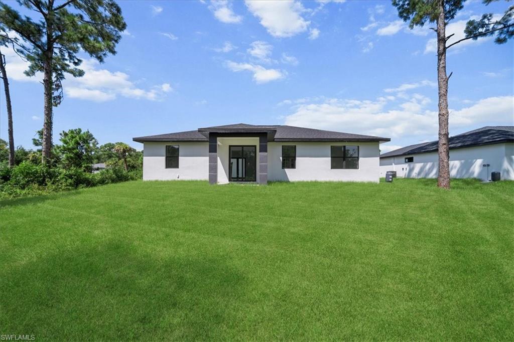 3315 67th Street West Lehigh Acres, FL 33971 - Photo 33 of 38 Back of house featuring a lawn and stucco siding