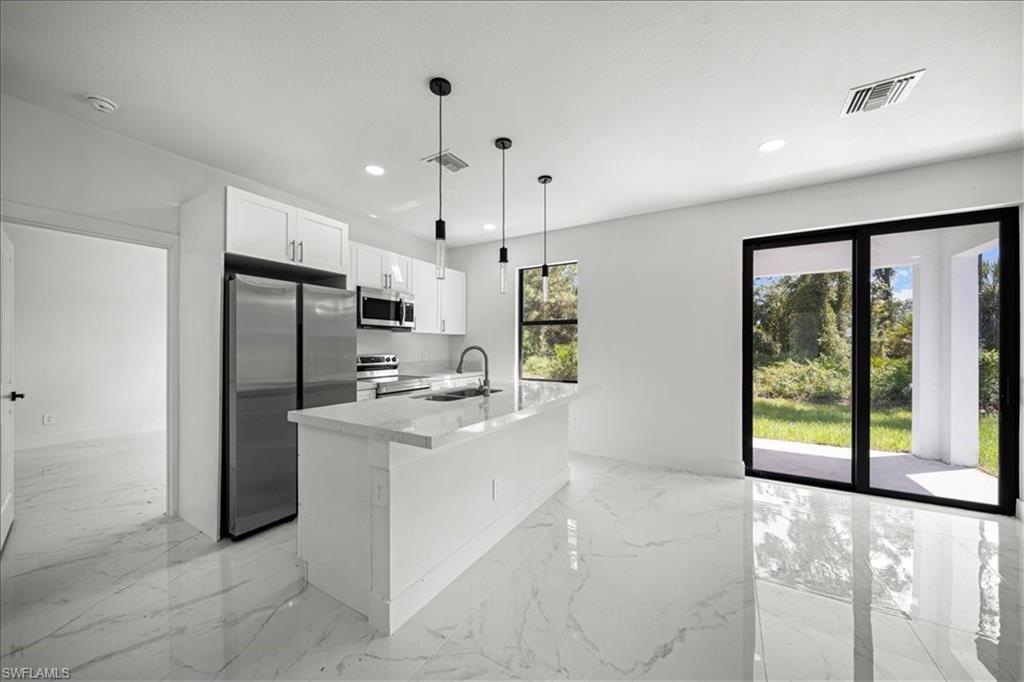 3315 67th Street West Lehigh Acres, FL 33971 - Photo 7 of 38 Kitchen featuring stainless steel appliances, hanging light fixtures, white cabinets, light stone countertops, and a kitchen island with sink