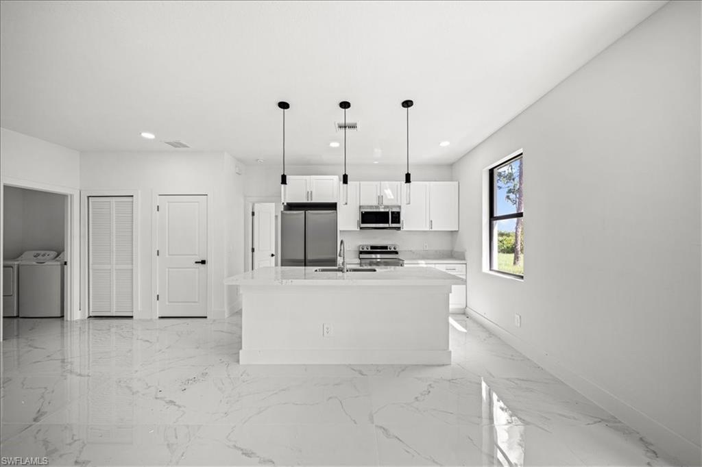 3315 67th Street West Lehigh Acres, FL 33971 - Photo 9 of 38 Kitchen featuring a kitchen island with sink, white cabinetry, stainless steel appliances, decorative light fixtures, and light marble finish floors