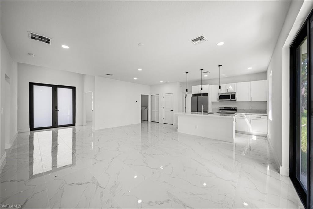 3315 67th Street West Lehigh Acres, FL 33971 - Photo 10 of 38 Kitchen featuring open floor plan, hanging light fixtures, white cabinetry, a center island with sink, and stainless steel appliances