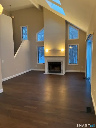 a view of an empty room with wooden floor fire place and a window