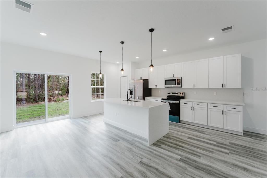6732 Southwest 132nd Street Ocala, FL 34473 - Photo 10 of 36 a kitchen with stainless steel appliances white cabinets a sink a stove a refrigerator and white walls with wooden floors