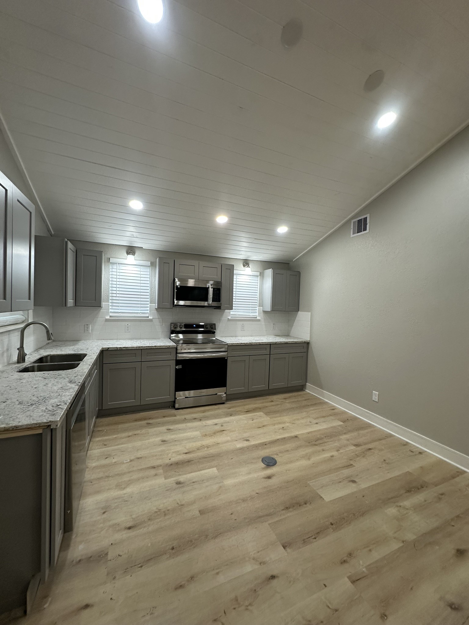 8223 Wallis Street Fulshear, TX 77441 - Photo 11 of 30 a large white kitchen with kitchen island a stove a sink a refrigerator and white cabinets with wooden floor