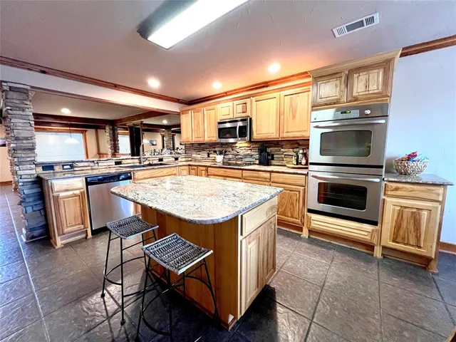 a view of a kitchen with kitchen island a large counter space a large window and stainless steel appliances