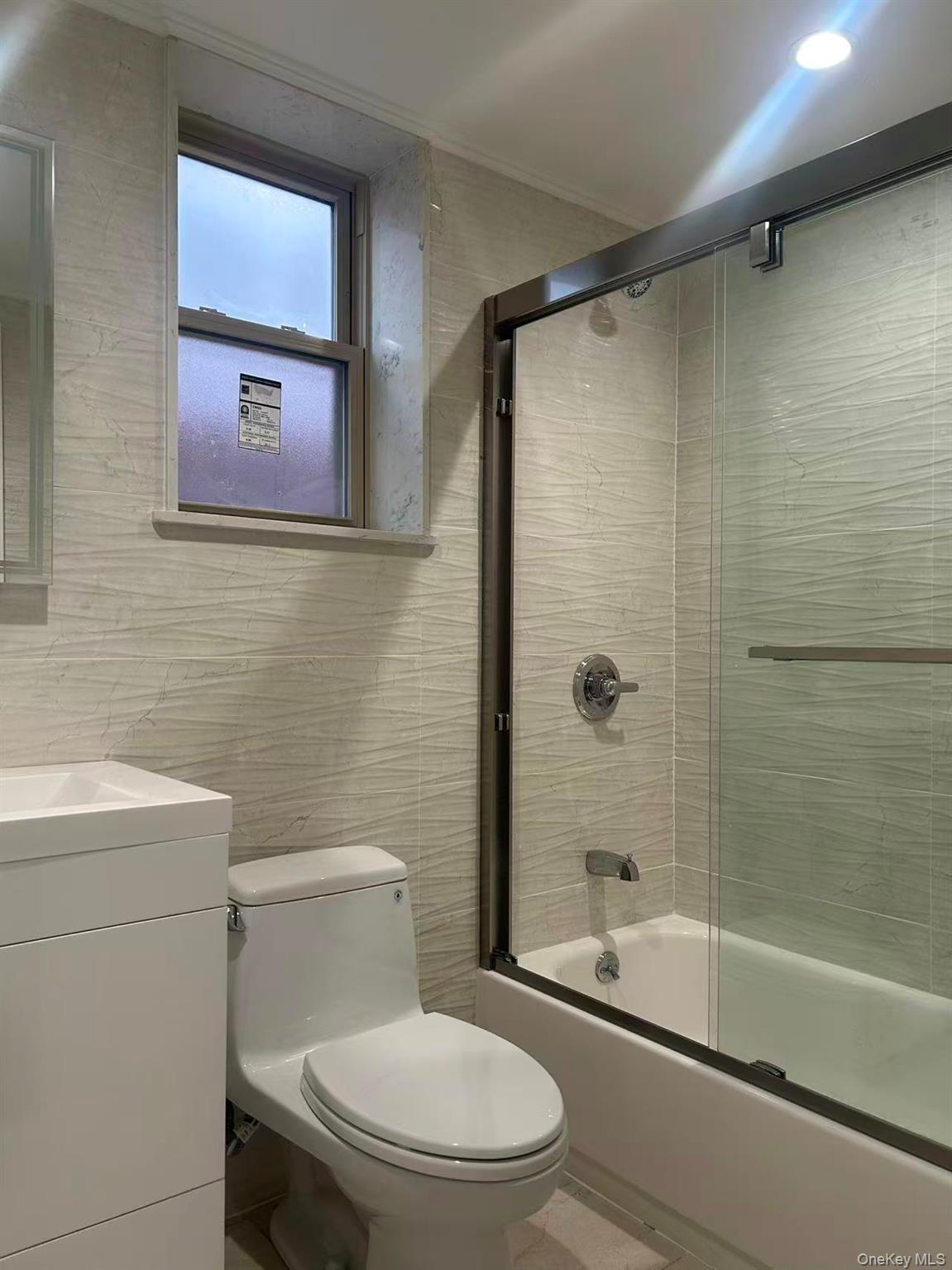 924 129th Street Queens, NY 11356 - Photo 22 of 23 Bathroom featuring bath / shower combo with glass door, tile walls, and vanity