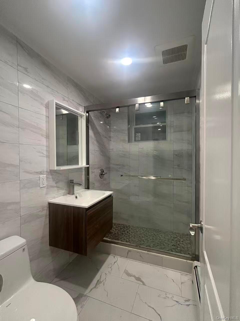 924 129th Street Queens, NY 11356 - Photo 23 of 23 Bathroom with a stall shower, vanity, light marble finish floors, and tile walls