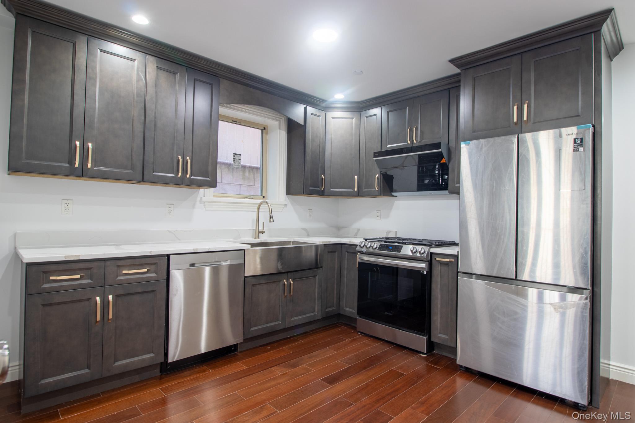 924 129th Street Queens, NY 11356 - Photo 3 of 23 Kitchen with stainless steel appliances, wood tiled floors, exhaust hood, light stone countertops, and dark brown cabinetry