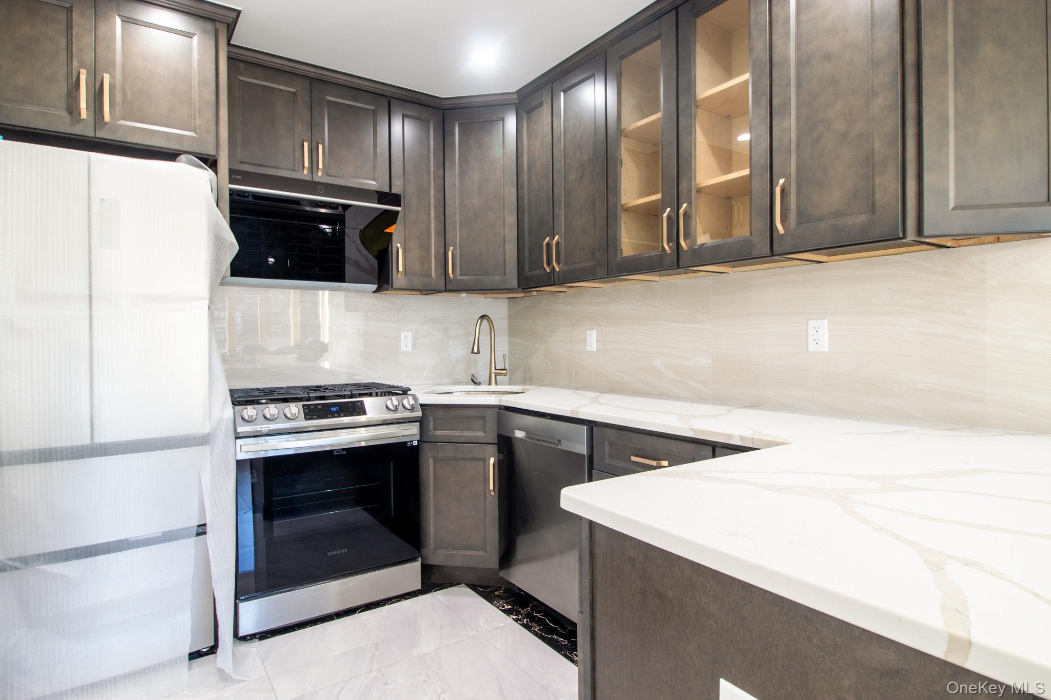 924 129th Street Queens, NY 11356 - Photo 5 of 23 Kitchen featuring dark brown cabinets, stainless steel appliances, glass insert cabinets, and light stone counters