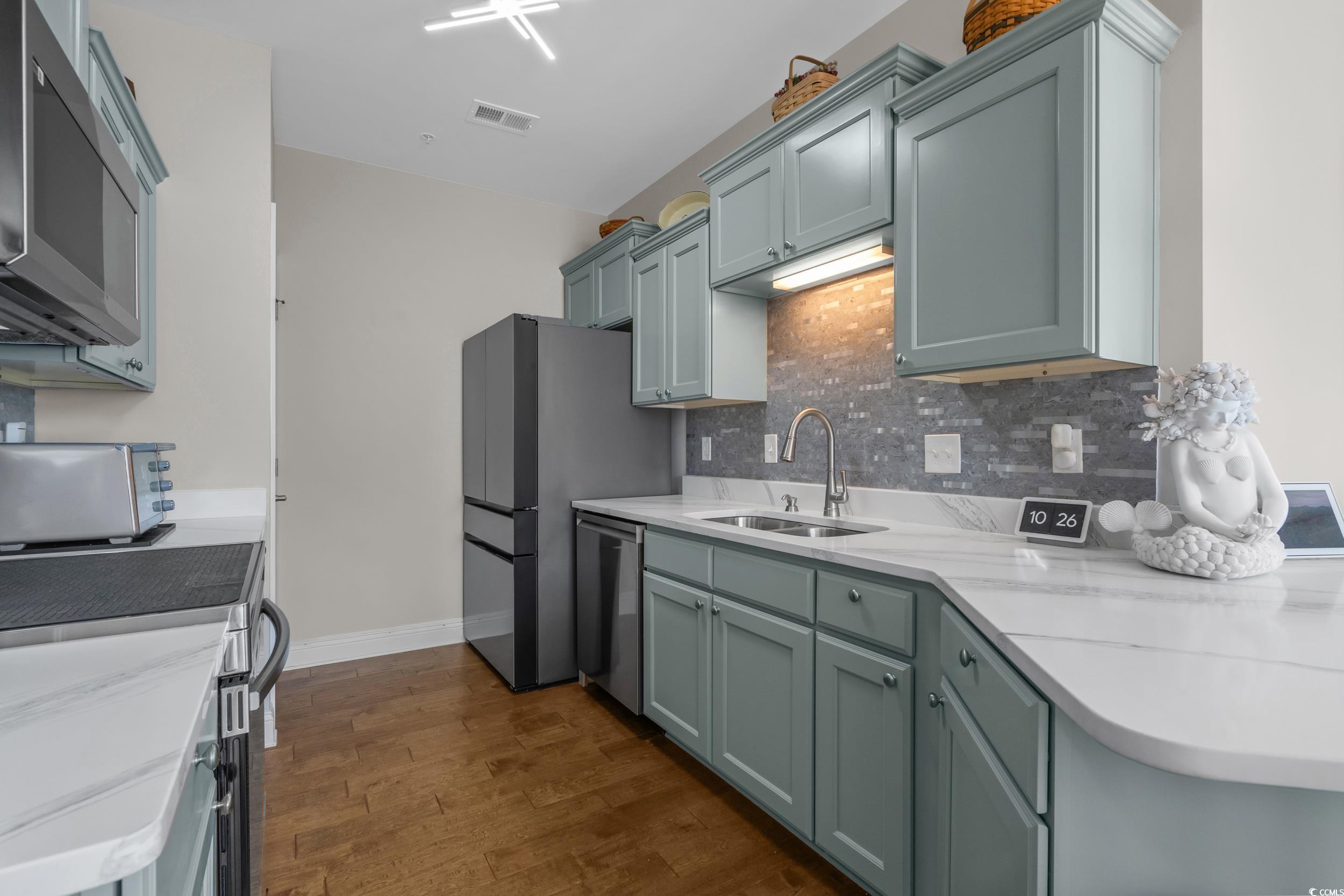 142 Ella Kinley Circle, Unit 304 Myrtle Beach, SC 29588 - Photo 17 of 38 Kitchen featuring stainless steel appliances, decorative backsplash, dark wood-style floors, and light stone countertops