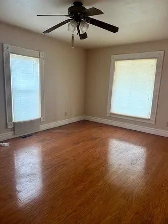 an empty room with wooden floor fan and windows