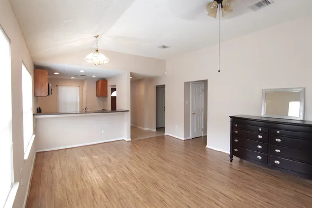 a view of an empty room and kitchen with wooden floor